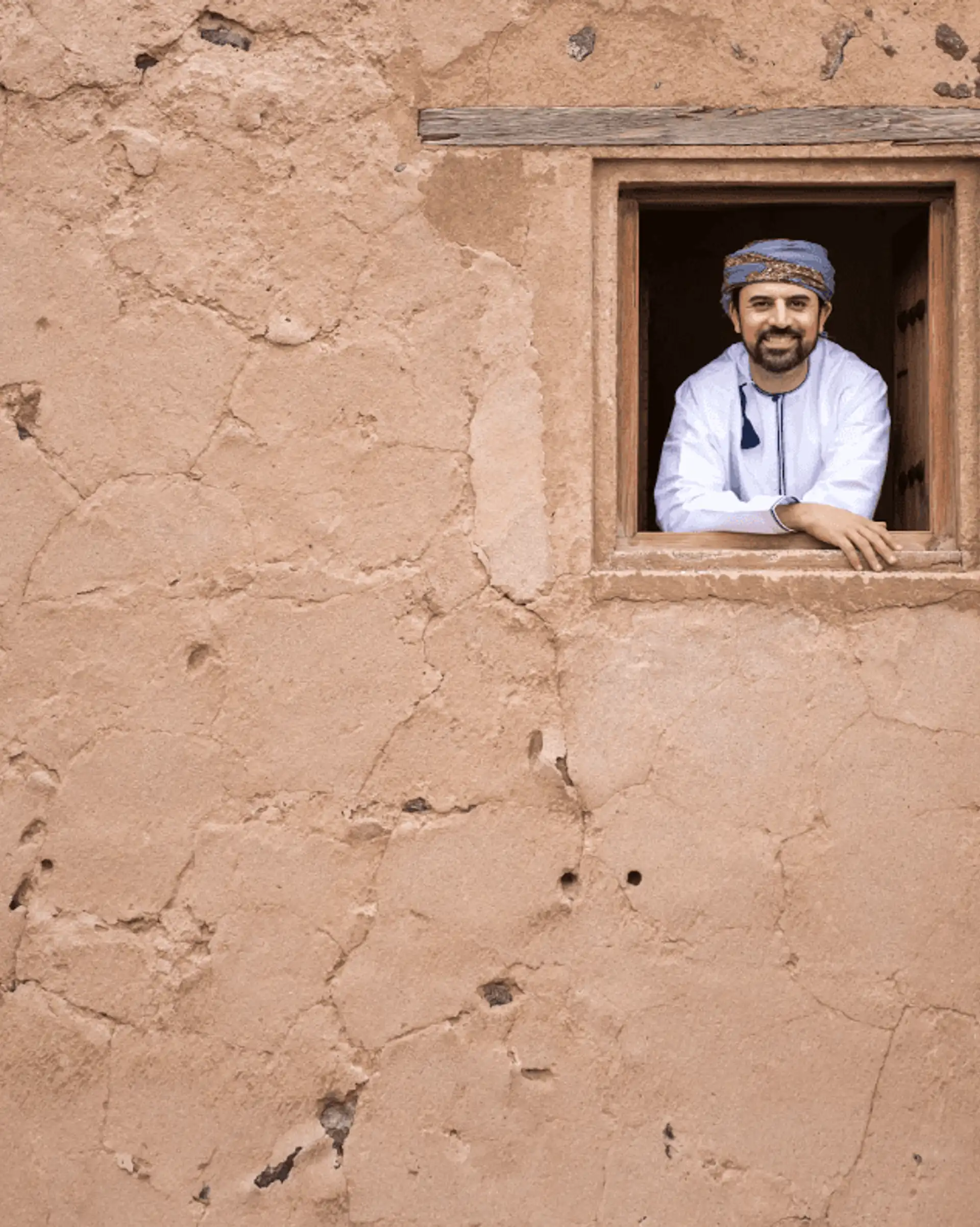 Homme omanais souriant à la fenêtre d'une maison traditionnelle en briques de terre à Oman