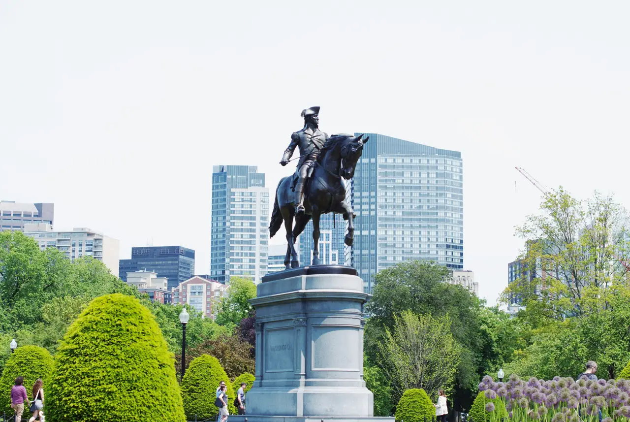 Statue équestre en bronze de George Washington entourée des arbres fleuris du Boston Public Garden devant les immeubles modernes de la ville