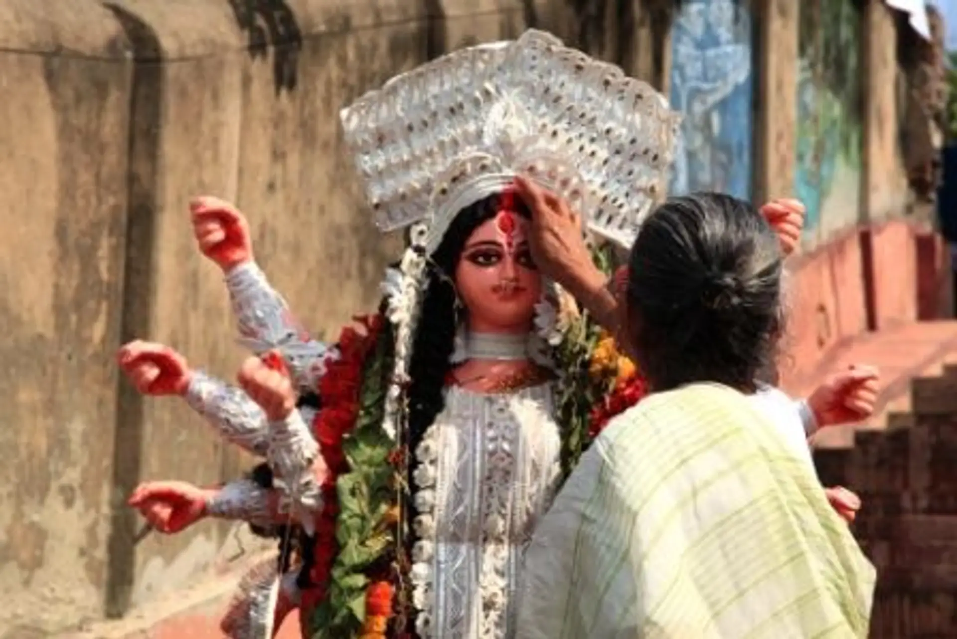 Travel in Asia - A woman applying a sindoor to the forehead of a statue at the Durga Puja festival in India