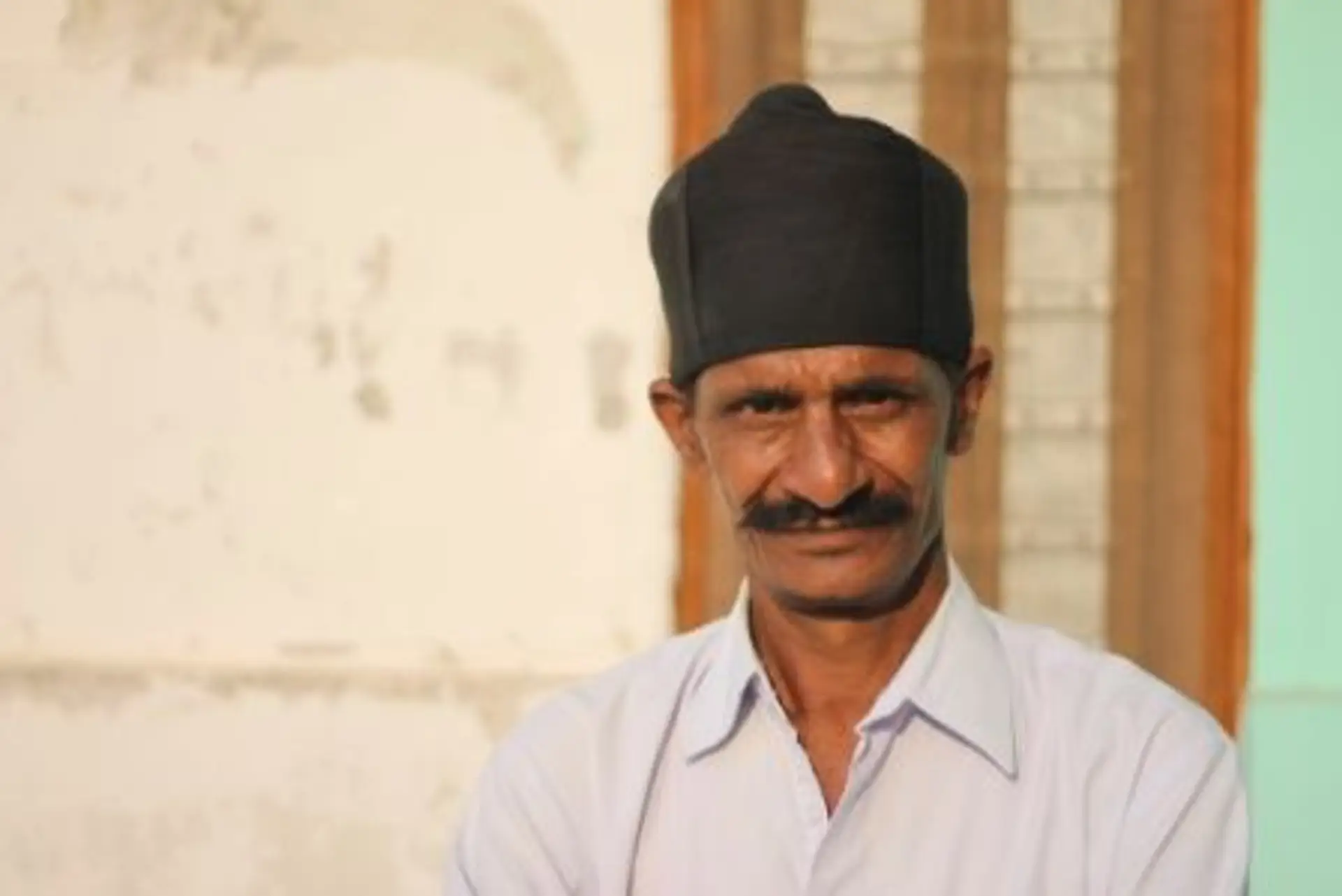 Travel in Asia - A man with a thick mustache and a black hat looking into the camera