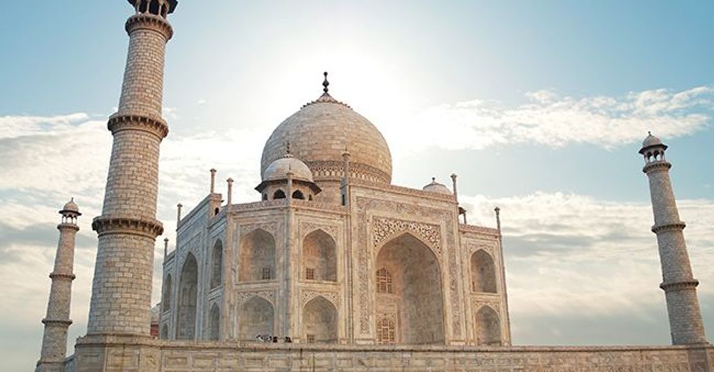 Voyage en Asie — Taj Mahal à Agra en Inde, mausolée de marbre blanc emblématique entouré de ses minarets sous un ciel clair.
