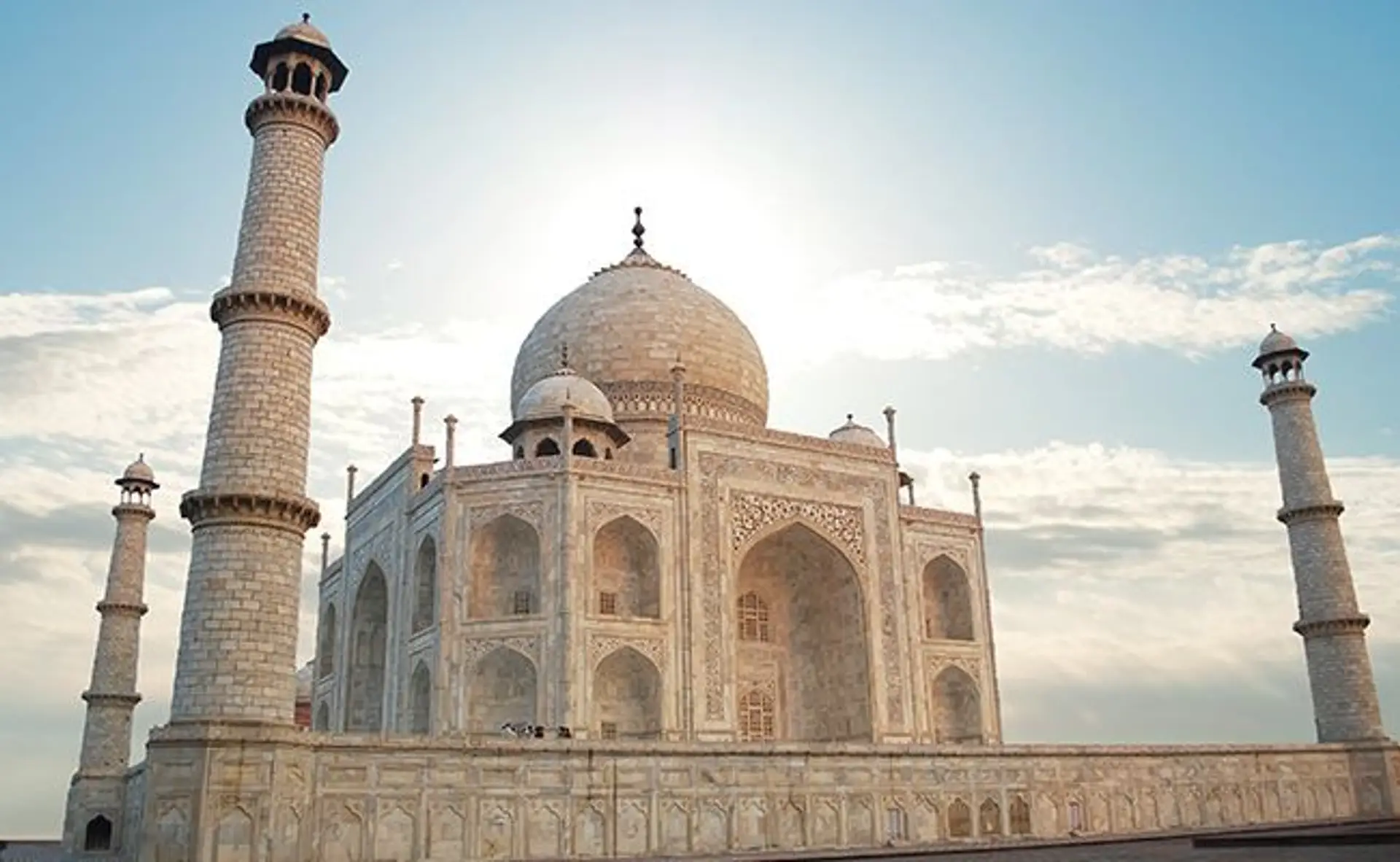 Voyage en Asie — Taj Mahal à Agra en Inde, mausolée de marbre blanc emblématique entouré de ses minarets sous un ciel clair.