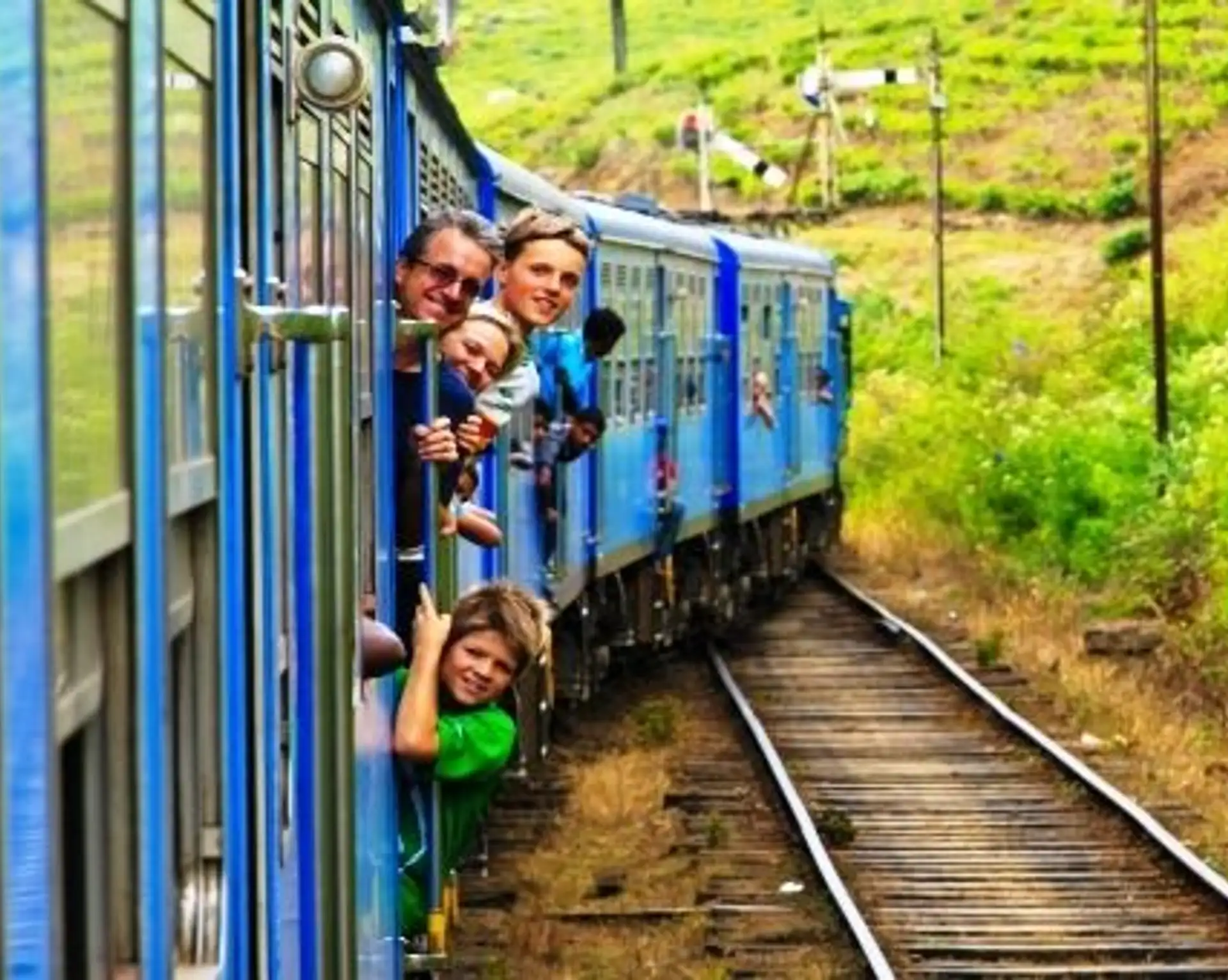 Voyageurs souriants regardant par les portes ouvertes du train bleu traversant les plantations de thé verdoyantes du Sri Lanka.