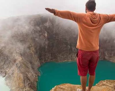 Travel in Asia - A man with outstretched arms standing on the edge of the crater of the Kelimutu volcano in Flores, Indonesia