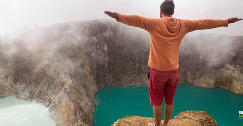 Travel in Asia - A man with outstretched arms standing on the edge of the crater of the Kelimutu volcano in Flores, Indonesia