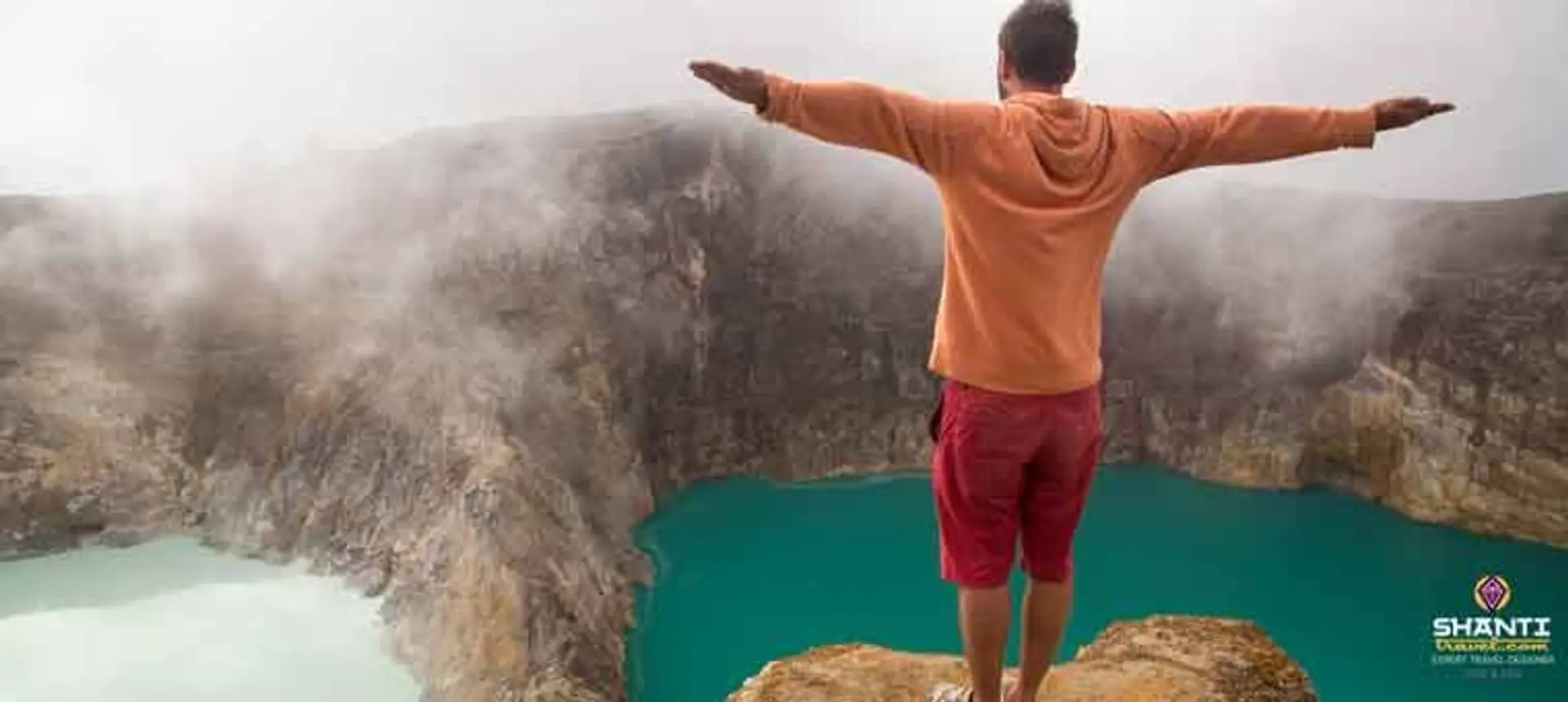 Travel in Asia - A man with outstretched arms standing on the edge of the crater of the Kelimutu volcano in Flores, Indonesia
