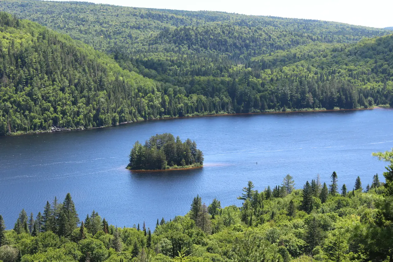 Vue plongeante sur un lac aux eaux sombres entouré d'une dense forêt boréale et de collines verdoyantes en Mauricie