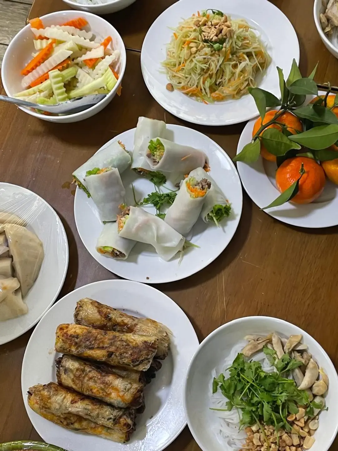 Une table en bois garnie de plats vietnamiens traditionnels avec des nems croustillants, des rouleaux de printemps frais, une salade de papaye verte et des agrumes.