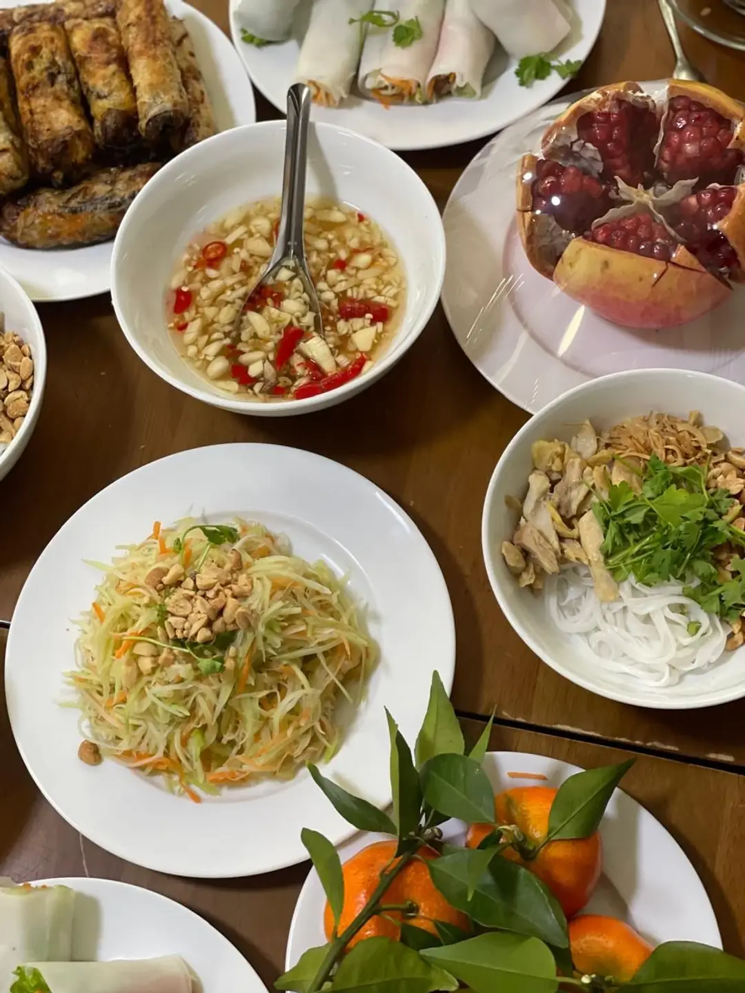 Gros plan sur des bols de nems, de salade de papaye aux cacahuètes, de vermicelles de riz au poulet et une grenade ouverte lors d'un repas au Vietnam.