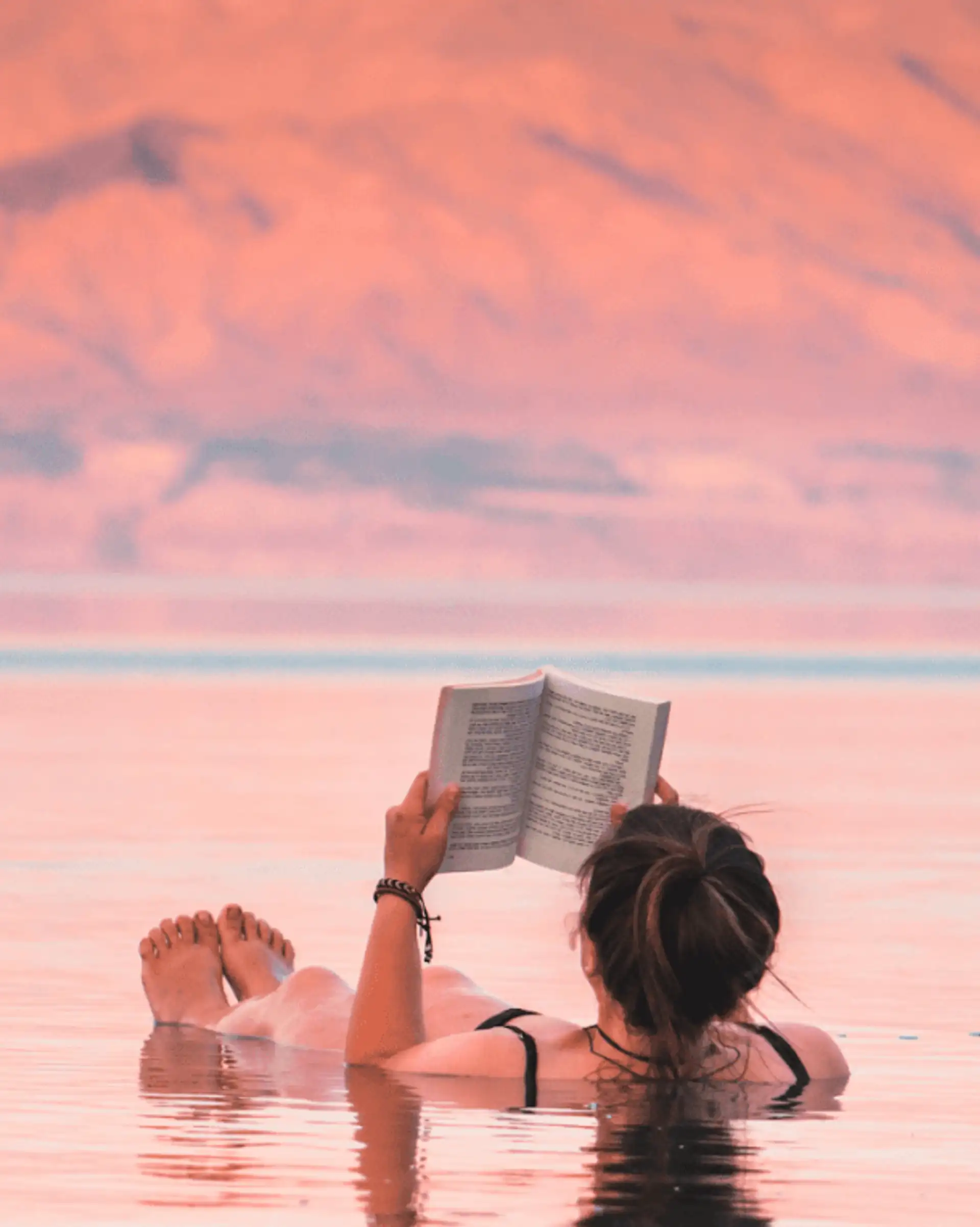 Voyage en Jordanie — Femme lisant un livre tout en flottant sur les eaux de la mer Morte au coucher du soleil.