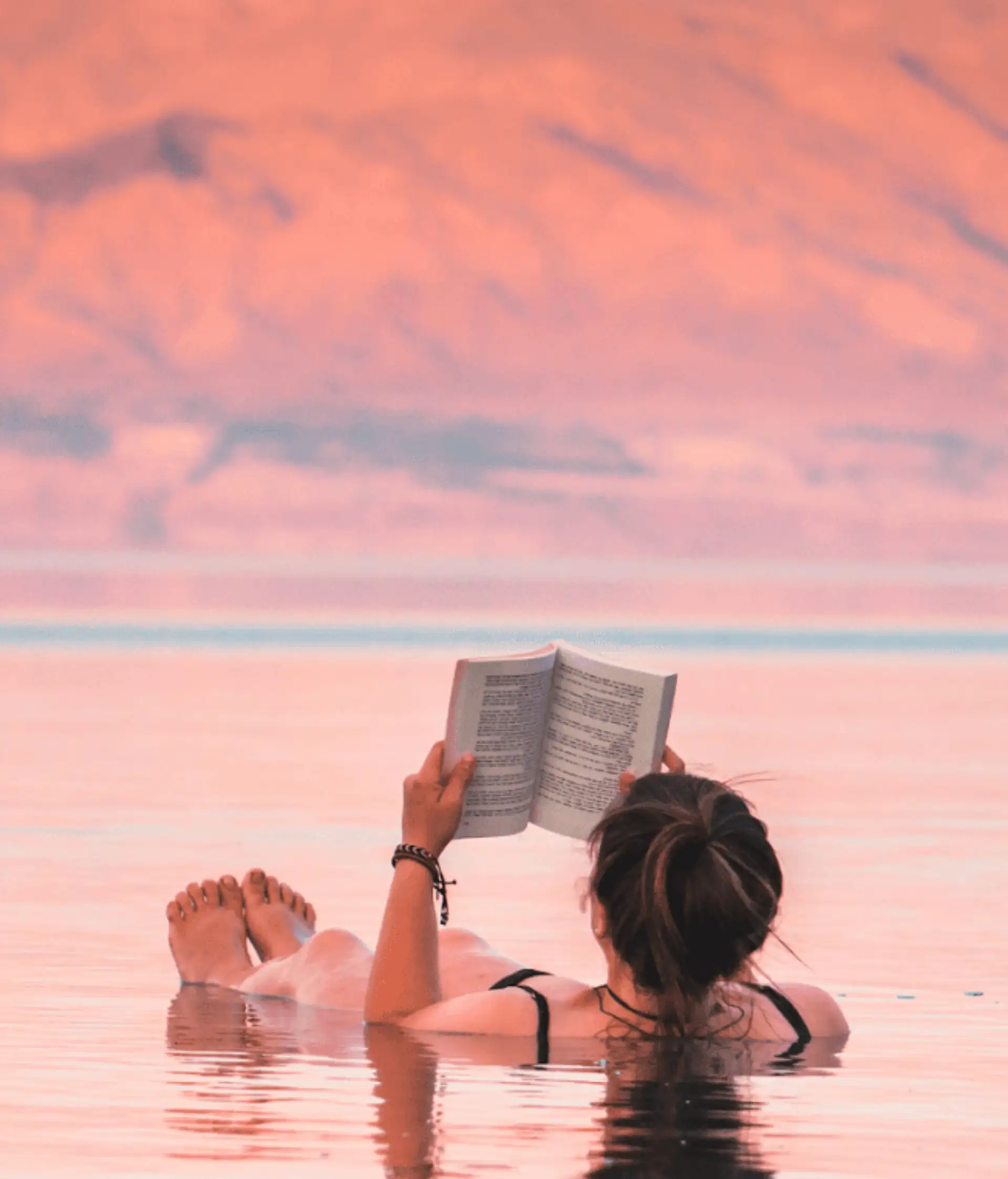 Voyage en Jordanie — Femme lisant un livre tout en flottant sur les eaux de la mer Morte au coucher du soleil.