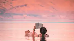 Voyage en Jordanie — Femme lisant un livre tout en flottant sur les eaux de la mer Morte au coucher du soleil.