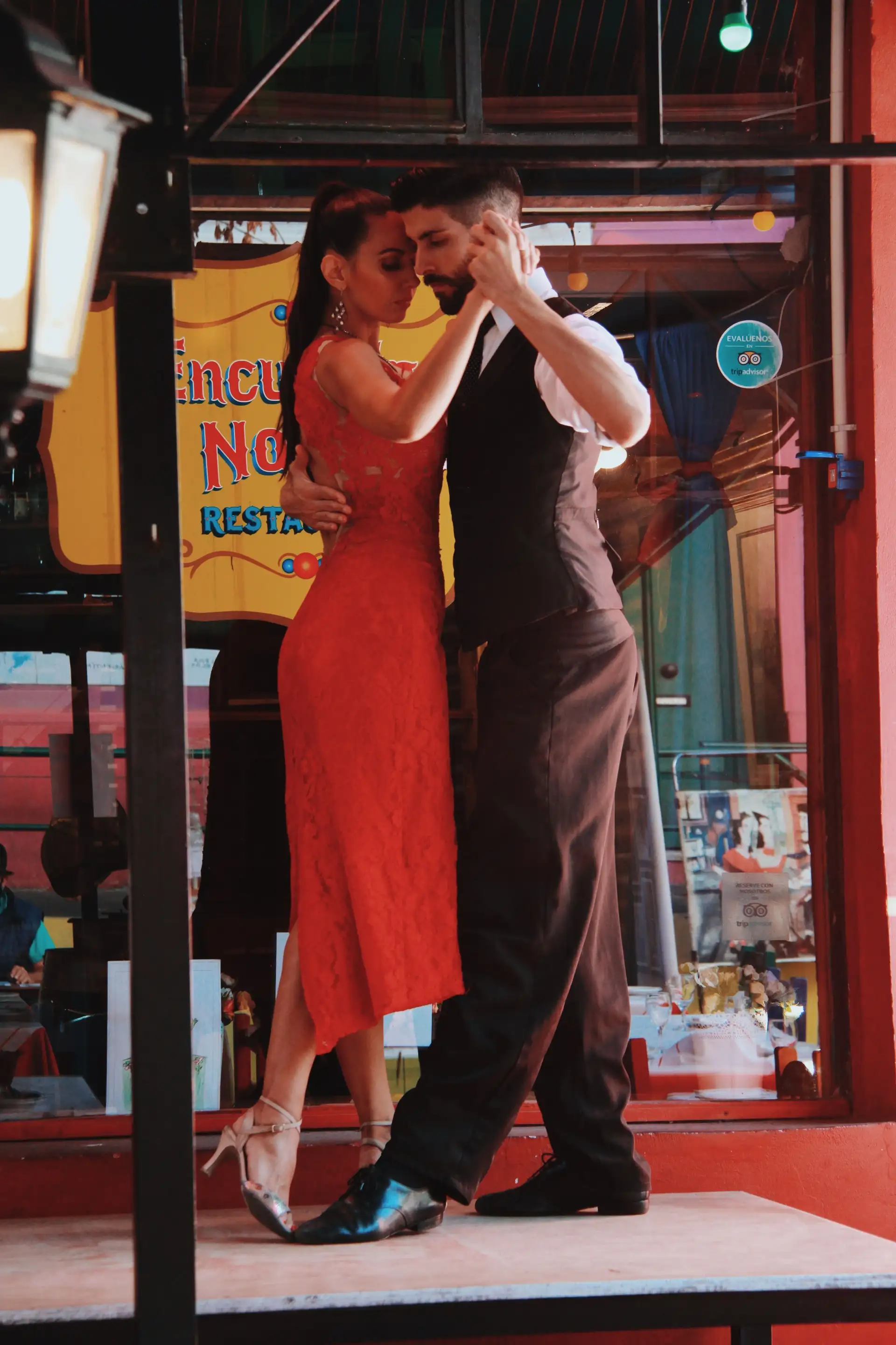 Voyage en Argentine – Un couple de danseurs de tango en tenue élégante effectuant une figure de danse dans une rue animée de Buenos Aires.