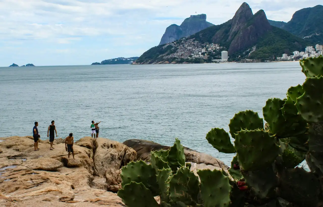 Voyage au Brésil en famille – Un groupe de voyageurs contemple l'océan depuis les rochers face à la plage d'Ipanema et la montagne des Deux Frères à Rio de Janeiro.