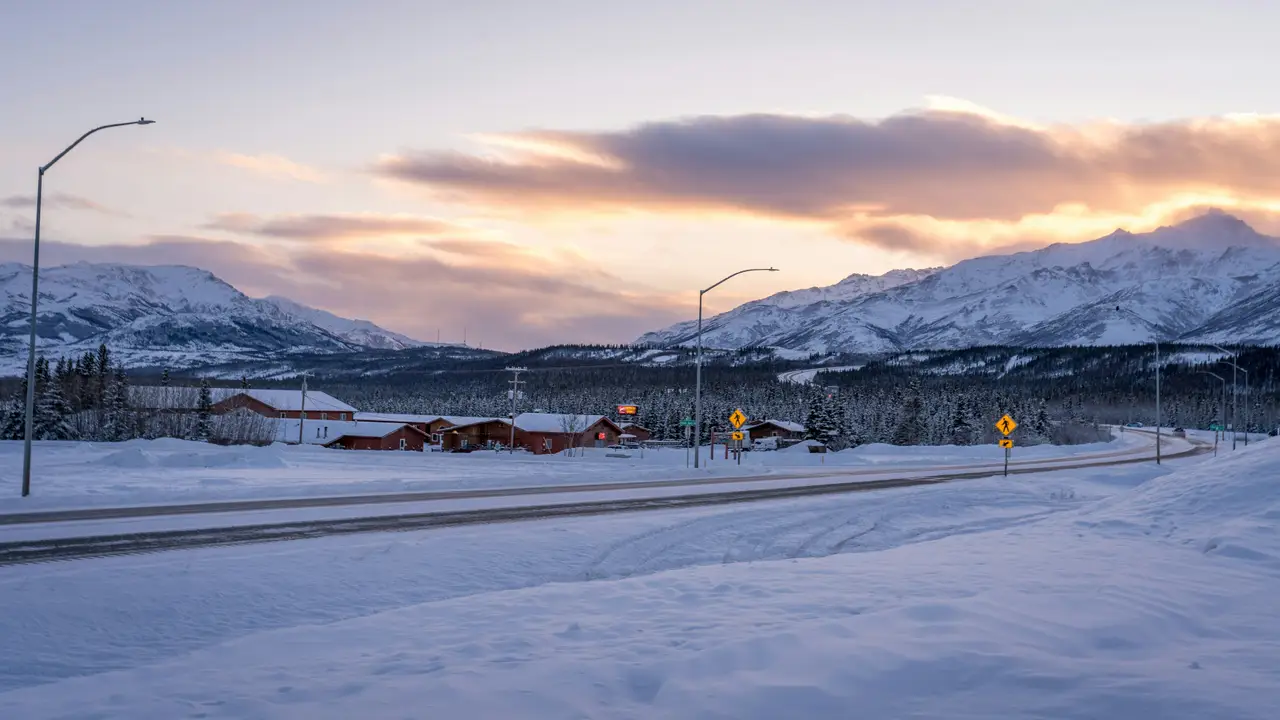 Route enneigée traversant un paysage d'hiver boréal au crépuscule avec des montagnes enneigées en arrière-plan entre Denali et Fairbanks