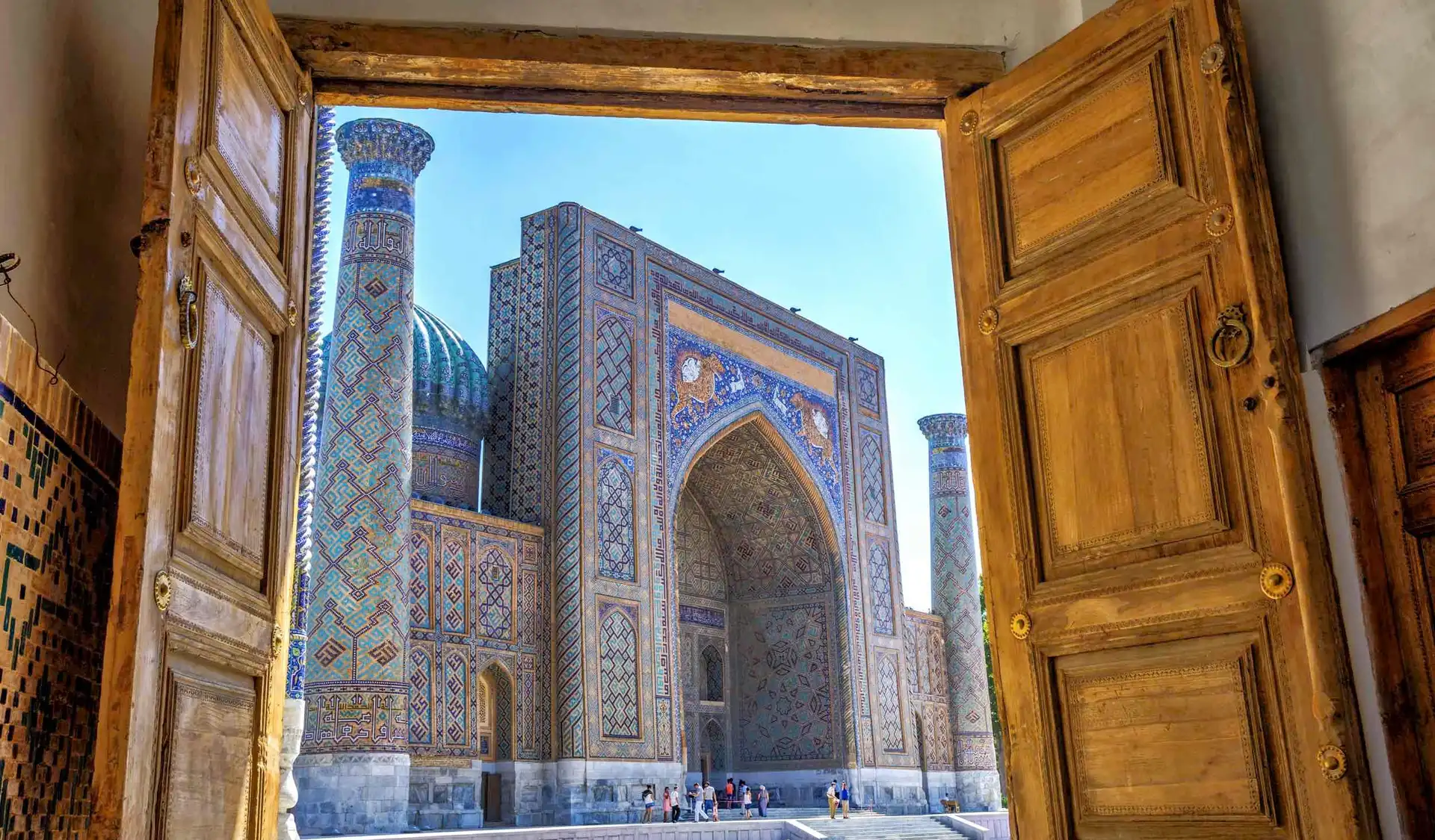 vue a travers une grande porte en bois ouverte sur la madrasa de samarcande avec ses minarets et ses mosaiques bleues en ouzbekistan