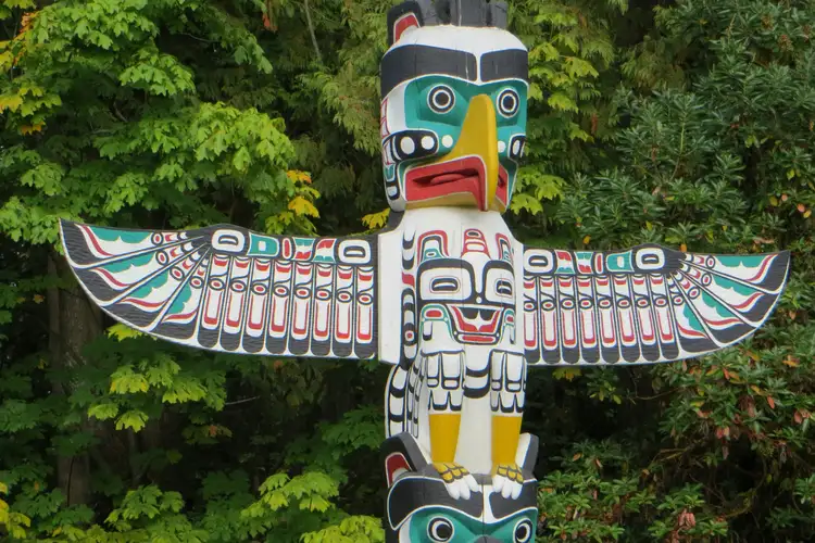 Mât totémique amérindien sculpté et peint aux motifs colorés dressé devant la verdure de Stanley Park à Vancouver