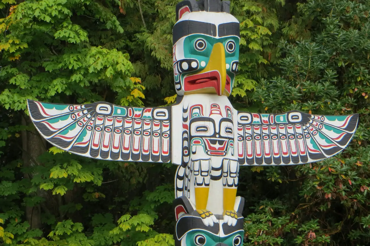 Mât totémique amérindien sculpté et peint aux motifs colorés dressé devant la verdure de Stanley Park à Vancouver