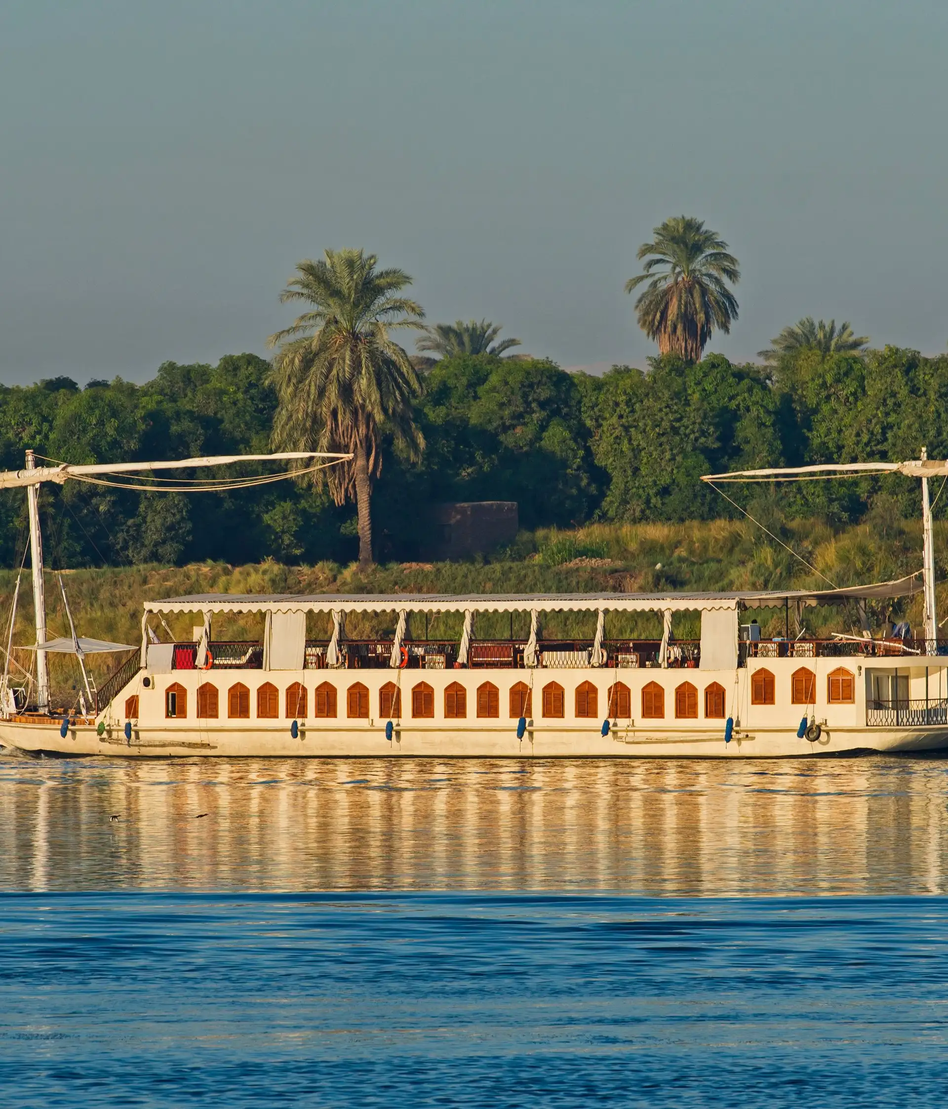 Dahabeya traditionnelle naviguant sur le Nil devant une rive bordée de palmiers