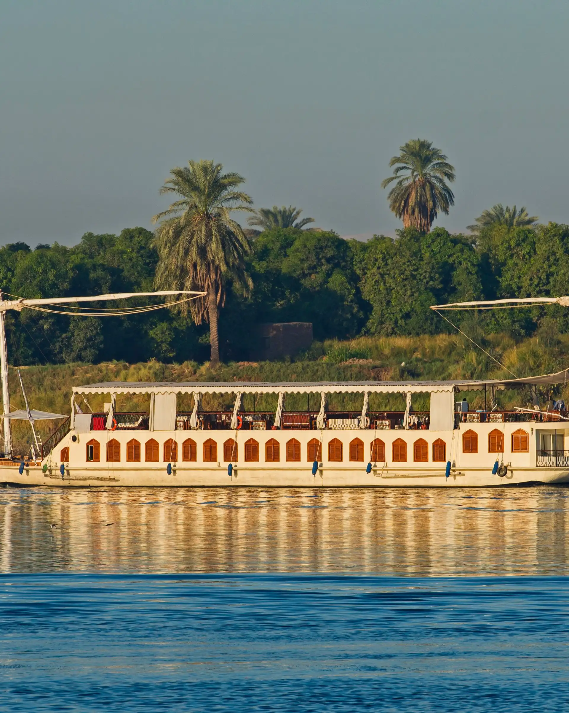 Dahabeya traditionnelle naviguant sur le Nil devant une rive bordée de palmiers