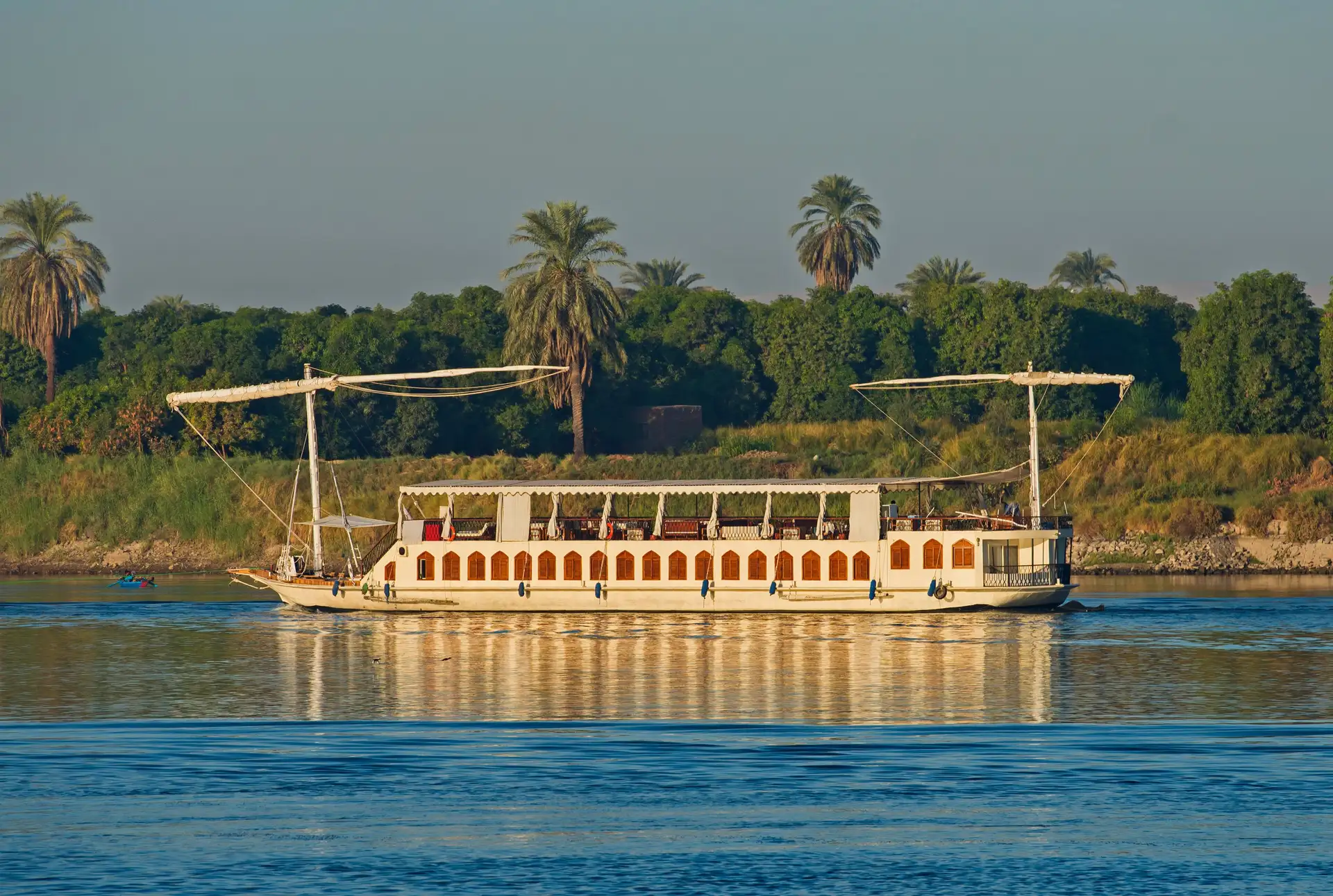 Dahabeya traditionnelle naviguant sur le Nil devant une rive bordée de palmiers