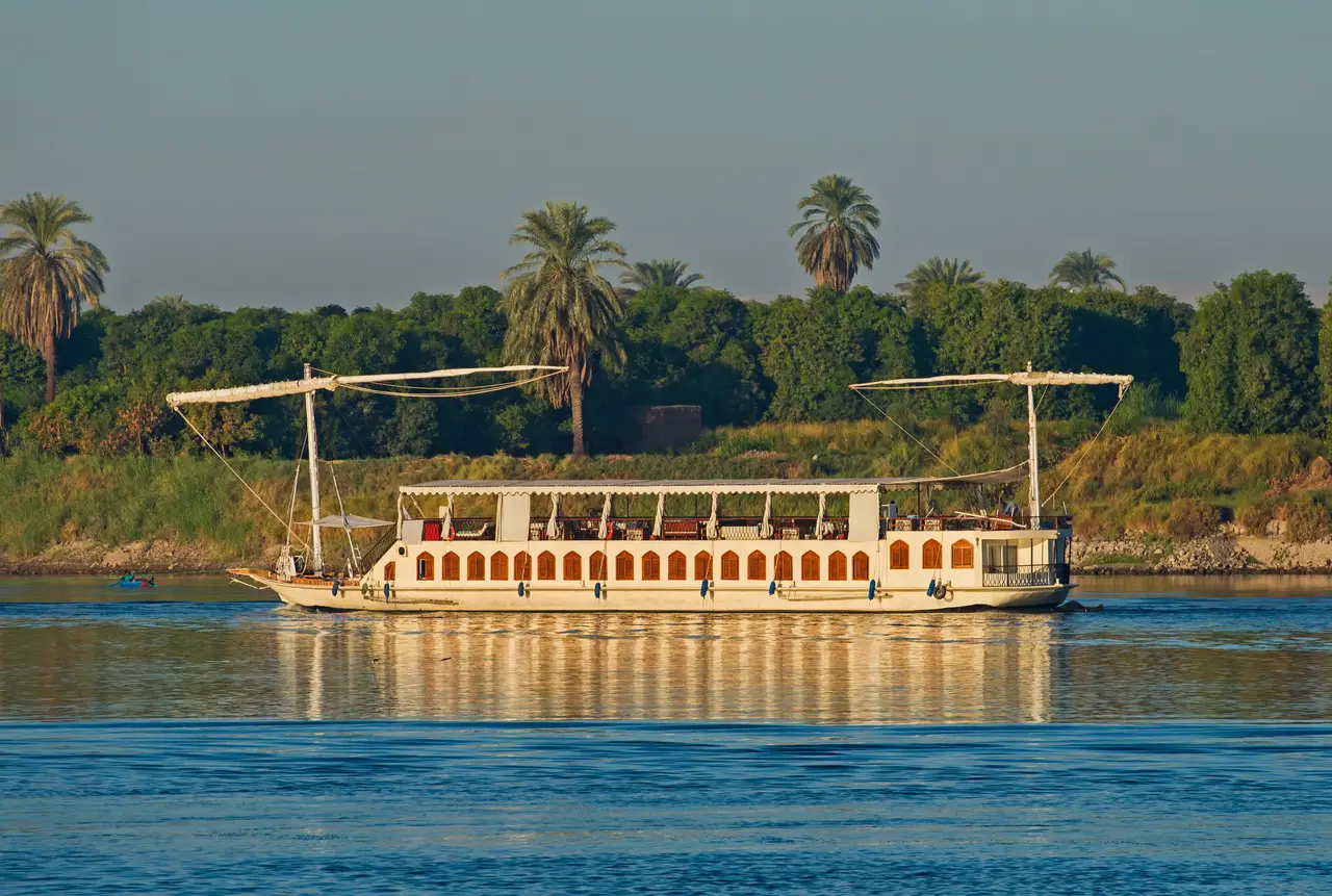 Dahabeya traditionnelle naviguant sur le Nil devant une rive bordée de palmiers