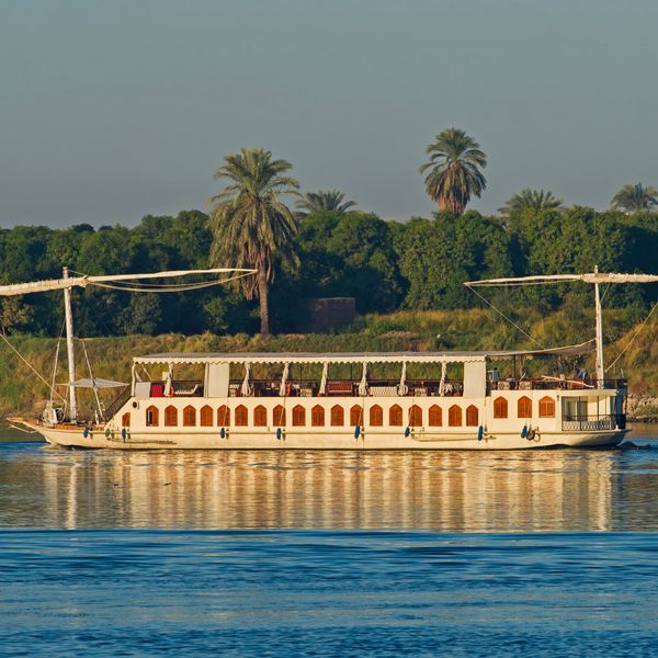 Dahabeya traditionnelle naviguant sur le Nil devant une rive bordée de palmiers
