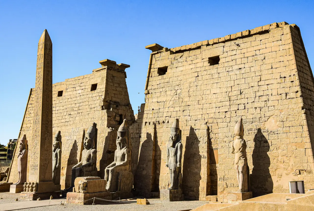 La façade monumentale du temple de Louxor présentant son obélisque solitaire, des statues assises de Ramsès II et des colosses debout devant un grand pylône en pierre