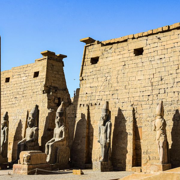 La façade monumentale du temple de Louxor présentant son obélisque solitaire, des statues assises de Ramsès II et des colosses debout devant un grand pylône en pierre