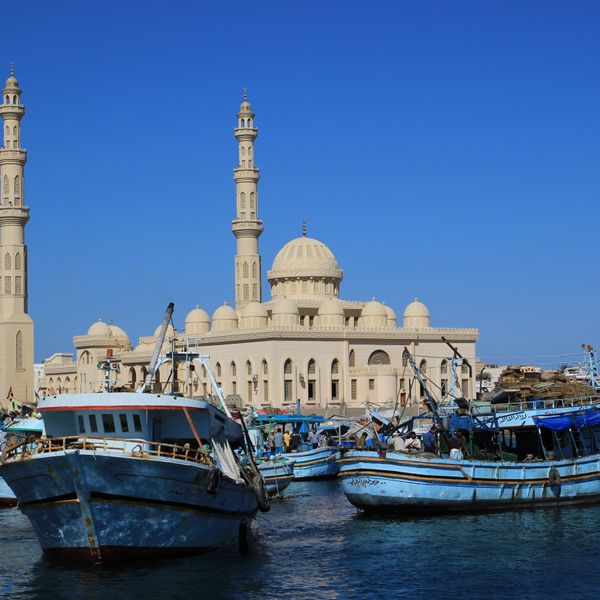 Plusieurs bateaux de pêche traditionnels amarrés dans le port d'Hurghada, avec une grande mosquée et ses minarets sculptés en arrière-plan sous un ciel bleu intense