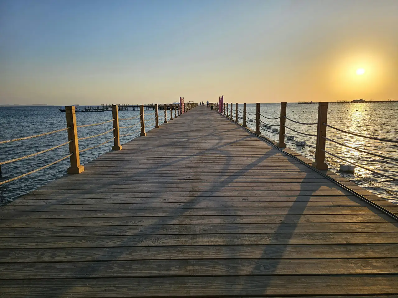 Un long ponton en bois s'avance sur la mer Rouge, où le soleil se couche