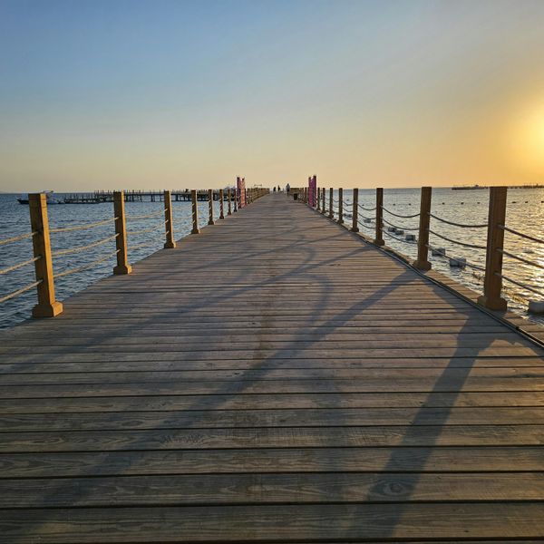 Un long ponton en bois s'avance sur la mer Rouge, où le soleil se couche