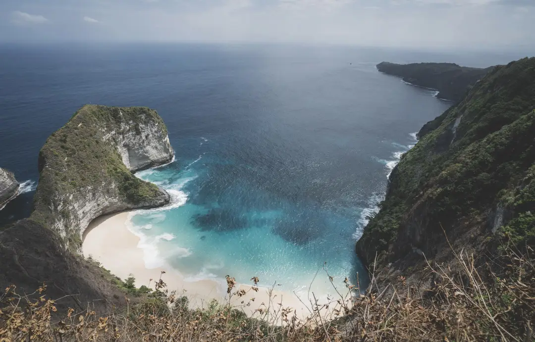 Voyage à Bali – Vue plongeante depuis la crête sur l'emblématique falaise en forme de T-Rex de Kelingking Beach et sa plage sauvage à Nusa Penida.