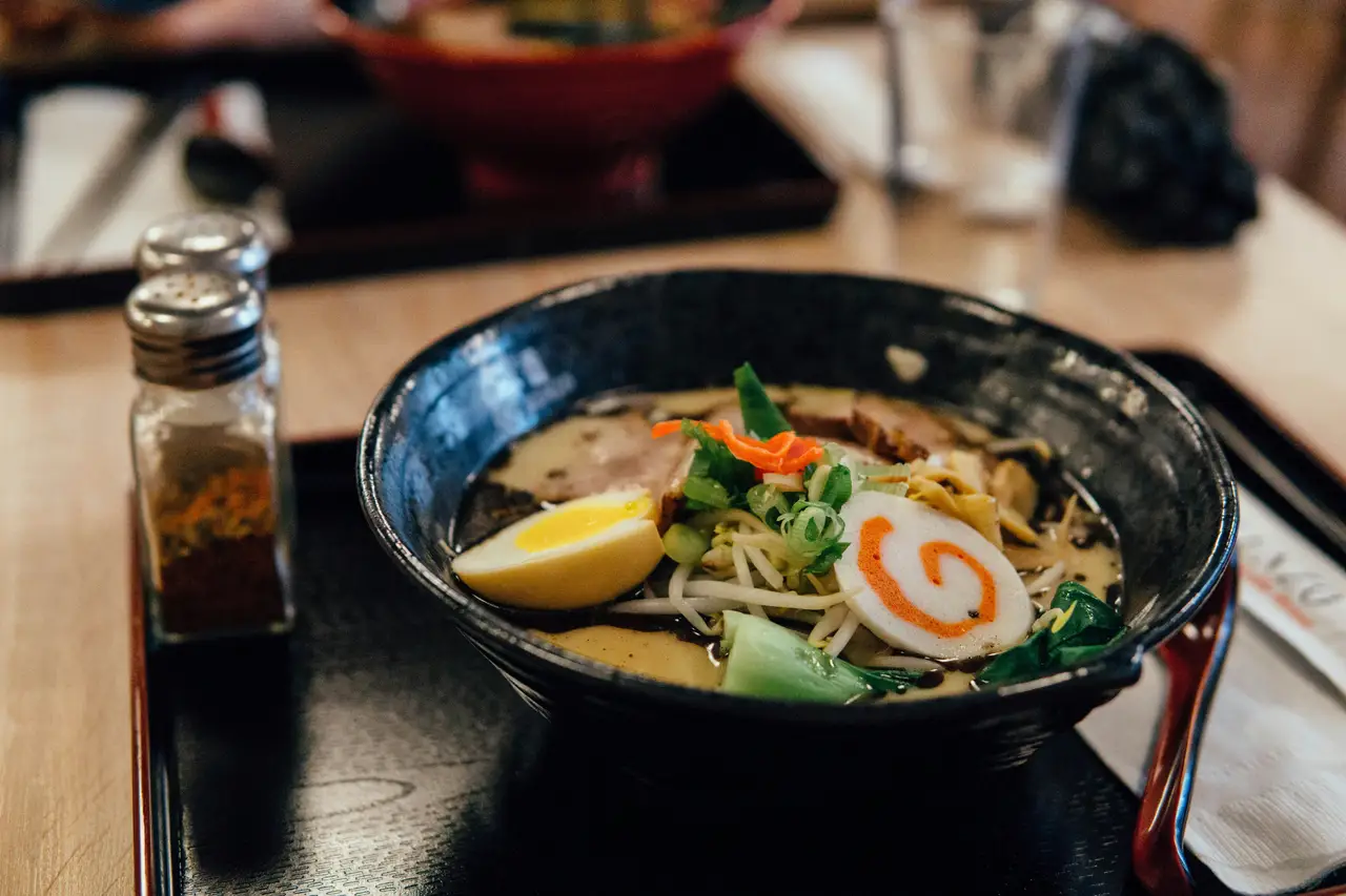 Un bol de ramen traditionnel fumant avec un œuf mollet, du narutomaki et des oignons verts, servi sur une table en bois dans un restaurant au Japon.