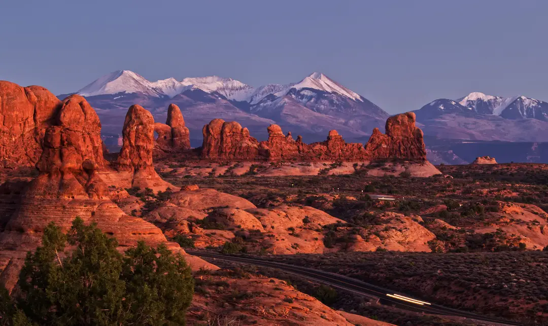 Formations rocheuses rouges et sommets enneigés au coucher du soleil dans le parc national des Arches, dans l’Utah.