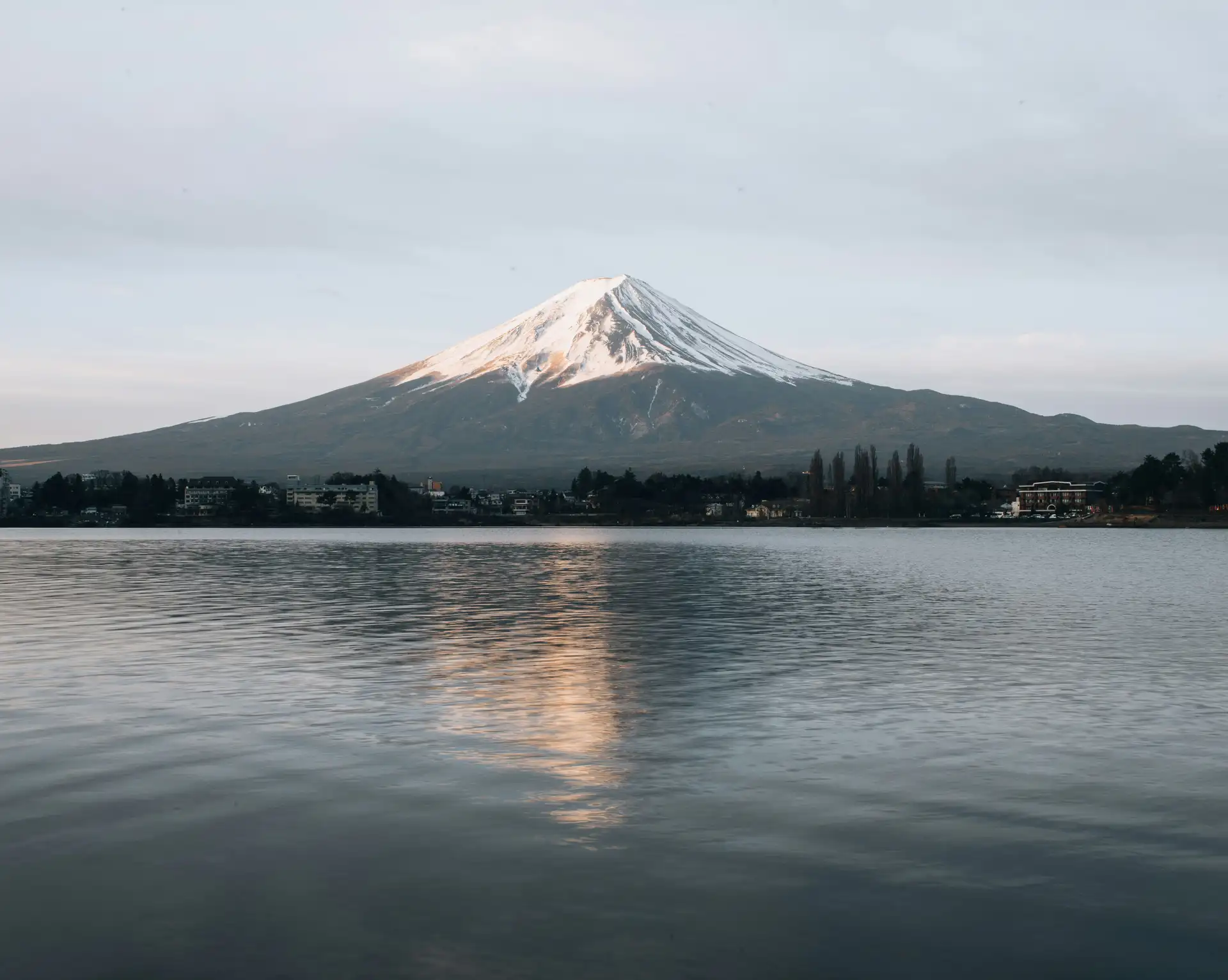 Le sommet enneigé du mont Fuji se reflétant sur les eaux calmes d'un lac entouré de végétation au lever du soleil au Japon.
