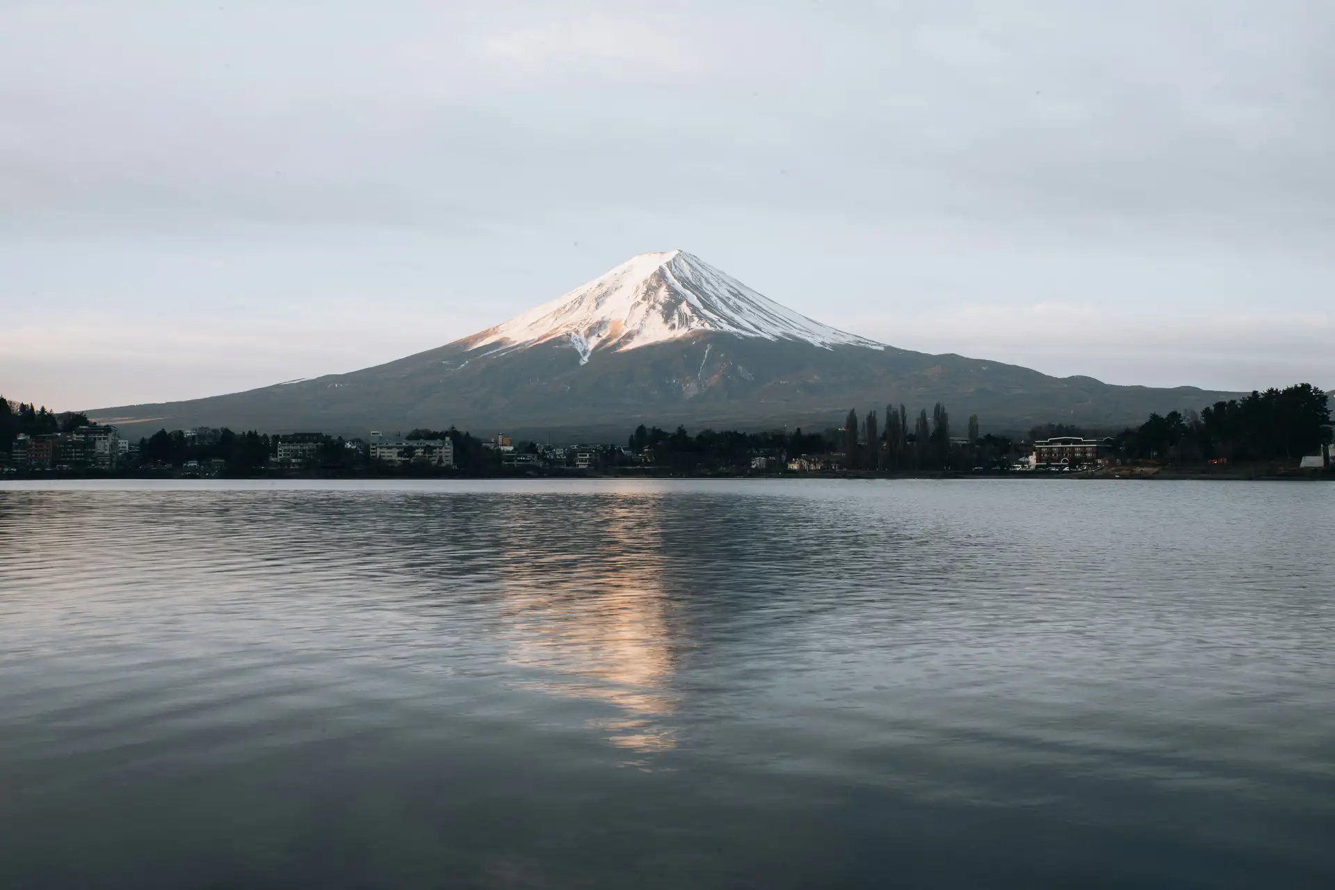 Le sommet enneigé du mont Fuji se reflétant sur les eaux calmes d'un lac entouré de végétation au lever du soleil au Japon.