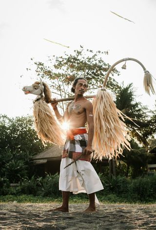 Voyage en Asie — Danseur balinais portant un masque et des accessoires traditionnels : silhouette en contre-jour et ambiance rituelle.