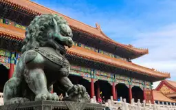 Statue de lion gardien traditionnel devant l'architecture impériale de la Cité Interdite à Pékin.