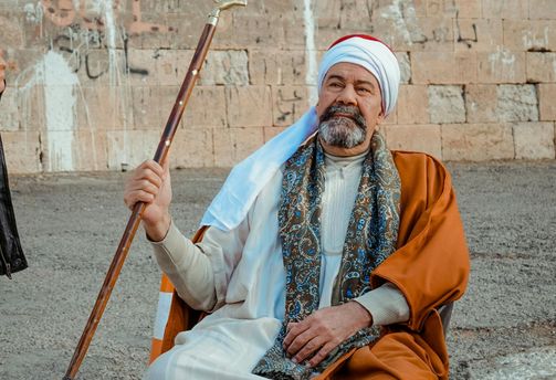 Voyage en Egypte - Homme en tenue traditionnelle assis avec une canne devant un mur en pierre