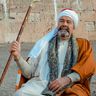 Voyage en Egypte - Homme en tenue traditionnelle assis avec une canne devant un mur en pierre