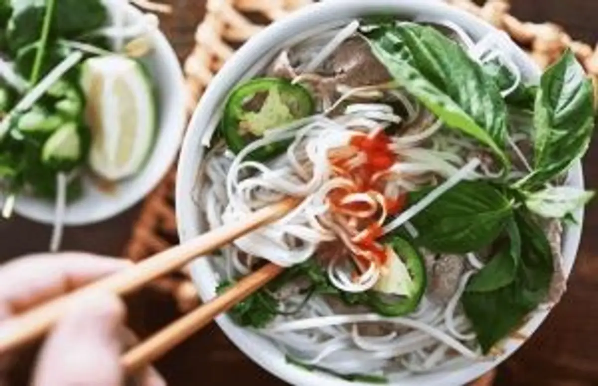 Travel in Asia - A person's chopsticks entering a bowl of pho with plenty of toppings