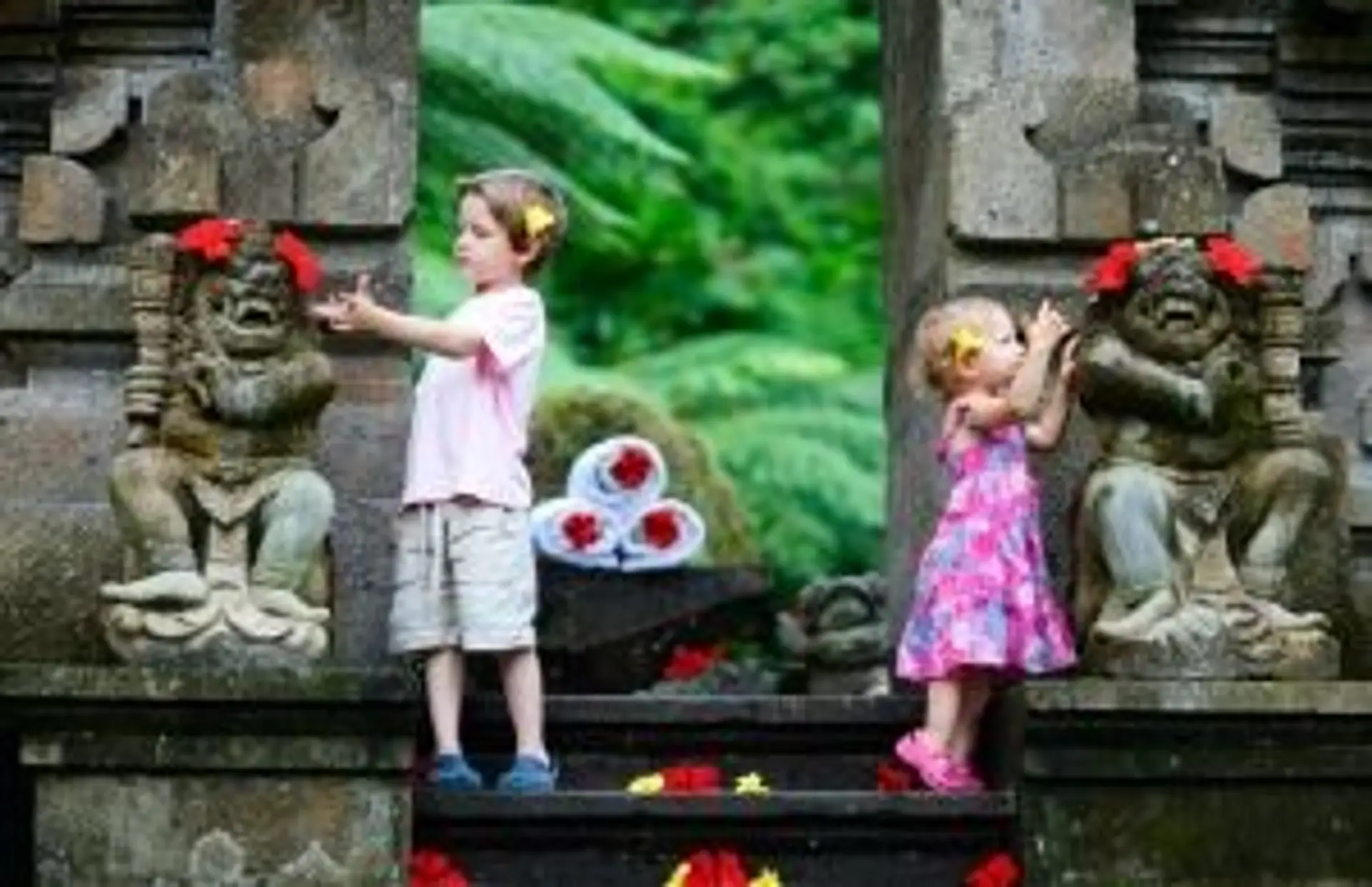 Deux jeunes enfants admirant des statues de gardiens balinais ornées de fleurs à l'entrée d'un temple