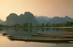 Voyage responsable au Laos — Barques traditionnelles sur une rivière paisible face aux montagnes de Vang Vieng.