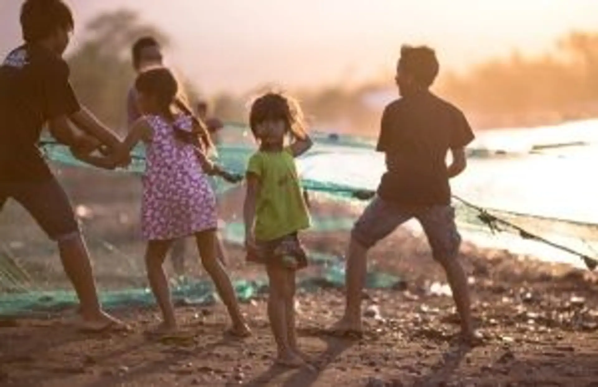 Enfants indonésiens aidant des pêcheurs avec leurs filets sur une plage au coucher du soleil