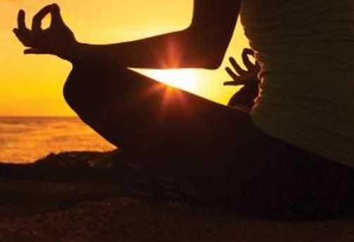 Travel in Asia - Person sitting in a meditative yoga pose, silhouetted against a sunset over water.