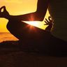 Travel in Asia - Person sitting in a meditative yoga pose, silhouetted against a sunset over water.