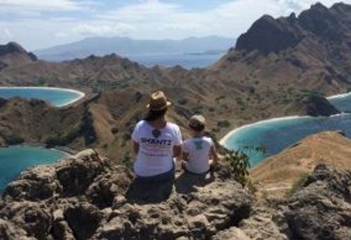 Travel in Asia - Two people sitting on a rocky summit looking over the landscape of Padar Island, part of Komodo National Park in Indonesia.