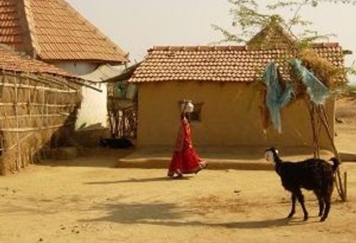 Travel in Asia - A woman and goat in a rural Indian village in front of a simple building with terracotta-tiled roofs