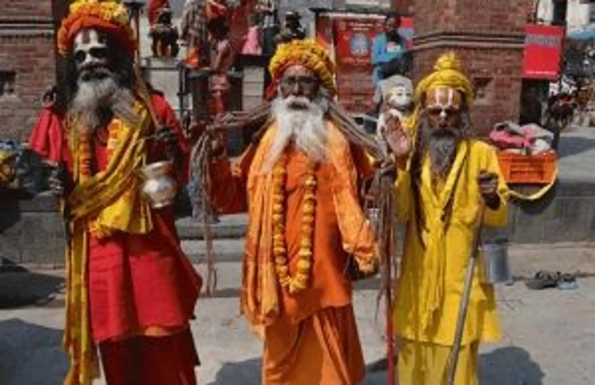 Trois Sadhus vêtus de tuniques orange et jaune avec des peintures faciales rituelles devant un temple au Népal.